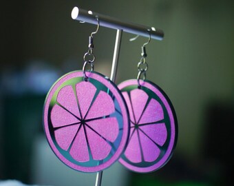 May include: A pair of pink and silver earrings shaped like a slice of citrus fruit. The earrings are hanging from a silver stand.