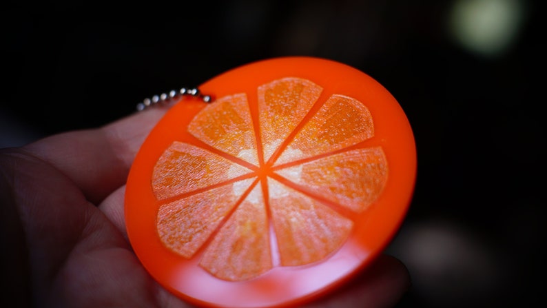 May include: A bright orange keychain shaped like a slice of orange with a silver chain.