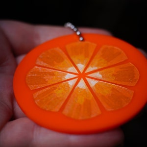May include: A bright orange keychain shaped like a slice of orange. The orange slice has a detailed design of segments and a white center.