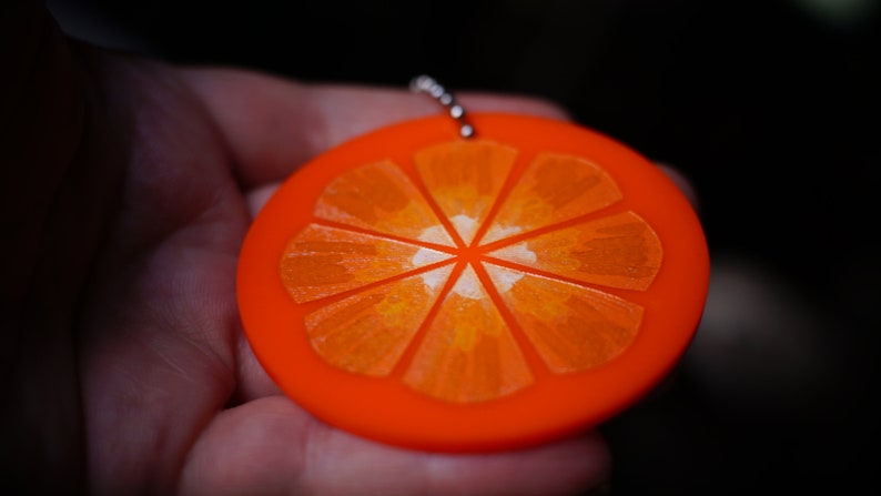 May include: A bright orange keychain shaped like a slice of orange. The orange slice has a detailed design of segments and a white center.