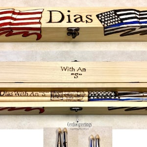 May include: A wooden box with a hinged lid, decorated with American and Thin Blue Line flags. The box contains two wooden drumsticks with the text "Dias With An "S"" engraved on them. The box is engraved with the text "Dias" and "With An "S"".