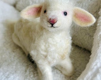 Pode incluir: Uma figurinha de cordeiro feita à mão, branca e fofa, com orelhas cor-de-rosa e olhos pretos. O cordeiro está sentado em uma superfície branca e fofa.