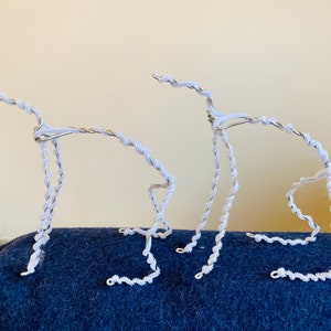 May include: Two white wire sculptures of stylized animals, possibly dogs, standing on a blue surface.