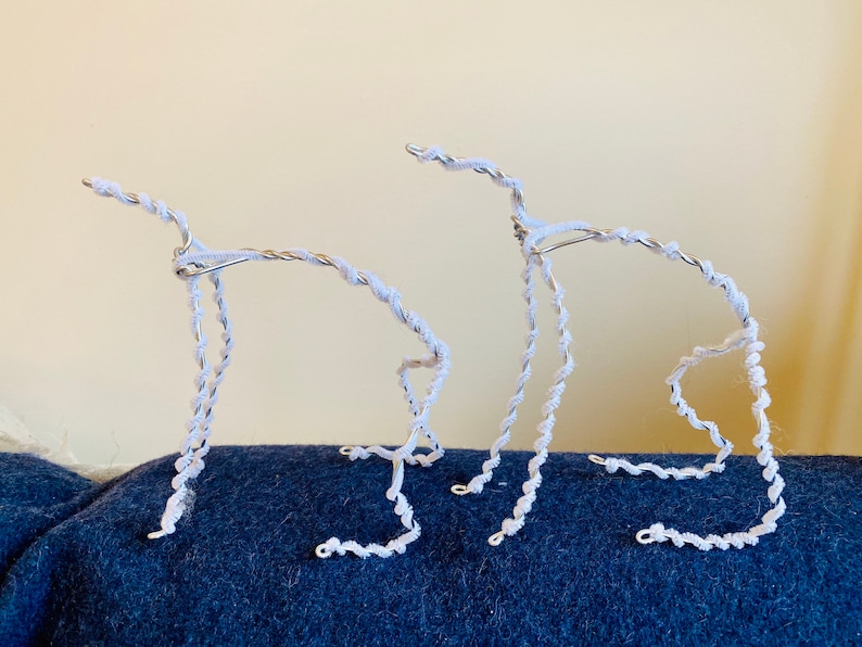 May include: Two white wire sculptures of stylized animals, possibly dogs, standing on a blue surface.