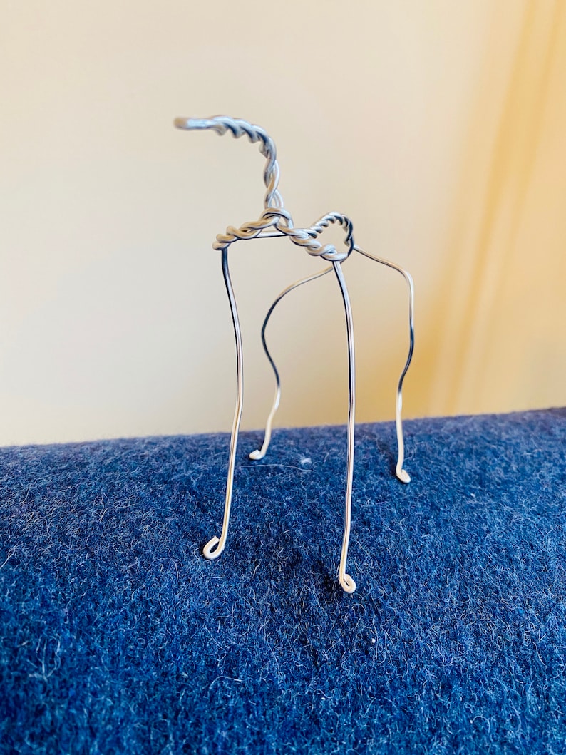 May include: A silver wire sculpture of a stylized animal with a long neck and four legs. The sculpture is standing on a blue surface.