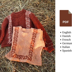 Pode incluir: Duas camisolas de malha, uma cor ferrugem e outra pêssego, com padrões florais. A camisola ferrugem tem mangas compridas, enquanto a pêssego é sem mangas. Ambas são feitas de fio texturizado e estão sobre feno.