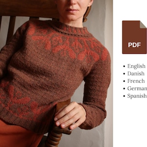 May include: A brown knit sweater with a floral design in orange on the yoke and lower chest. The sweater has long sleeves and a crew neck. A PDF icon is visible on the right side of the image, with a list of languages below it.