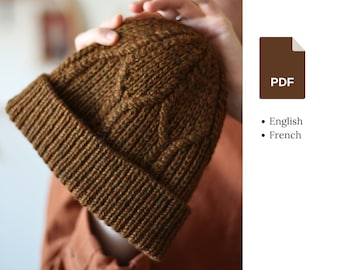 May include: A brown and green knitted beanie with a cable knit pattern. The beanie is folded down to create a cuff.