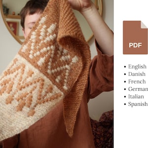 May include: A triangular knitted shawl featuring a two-tone color scheme of rust orange and cream. The design incorporates a textured geometric pattern with raised stitches. A brown PDF icon is displayed alongside a list of available languages.