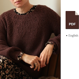 Può includere: Un maglione di lana marrone con un motivo di pizzo intorno al collo. Il maglione è indossato da una persona ed è mostrato frontalmente.