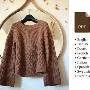 Könnte beinhalten: Ein brauner Strickpullover mit Zopfmuster. Der Pullover hat einen runden Ausschnitt und lange Ärmel.