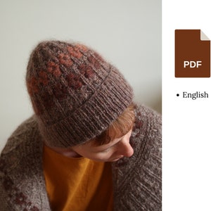 May include: A brown and pink knit beanie hat with a textured pattern. The hat is made of a soft, fuzzy yarn.