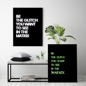 May include: Two black framed prints with the text "BE THE GLITCH YOU WANT TO SEE IN THE MATRIX" in white and green text. The prints are hanging on a white wall above a concrete table with a potted plant and two smaller potted plants.