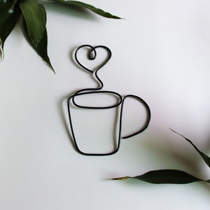 Könnte beinhalten: Eine schwarze Drahtskulptur einer Kaffeetasse mit einem herzförmigen Dampf, der aus ihr aufsteigt.