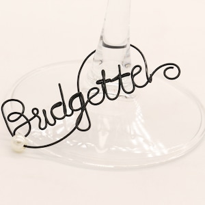 Op de afbeelding: Zwarte draad wijn glas charme met het woord "Bridgette" en een witte parel accent.