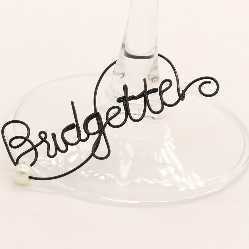 Op de afbeelding: Zwarte draad wijn glas charme met het woord "Bridgette" en een witte parel accent.