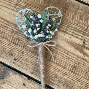 Puede incluir: Un ramo de flores secas en forma de corazón, que incluye aliento de bebé blanco y lavanda púrpura, atado con cordel y unido a un tallo largo de cordel marrón.