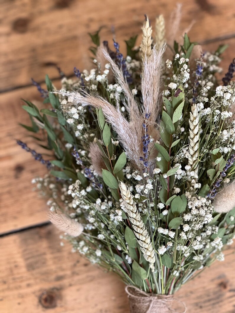 Puede incluir: Un ramo de flores secas con aliento de beb&eacute; blanco, tallos de trigo, lavanda y hierba de la pampa atados con cuerda.