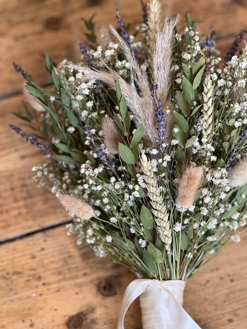 Puede incluir: Un ramo de flores secas con aliento de beb&eacute; blanco, lavanda seca, trigo y hierba de la pampa marr&oacute;n claro y esponjosa, atado con una cinta de sat&eacute;n blanca.