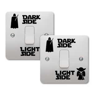 May include: Two white light switch covers with black vinyl decals. The top switch cover has a Darth Vader silhouette and the text "DARK SIDE". The bottom switch cover has a Yoda silhouette and the text "LIGHT SIDE".