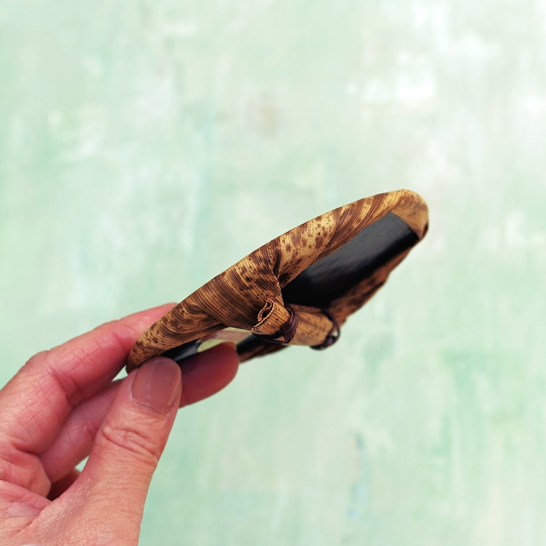 May include: A small, round, woven tray with a dark brown interior. The tray is made of natural materials and has a rustic, hand-crafted look.