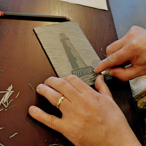 lino cut process - a mans hand cutting a lighthouse design