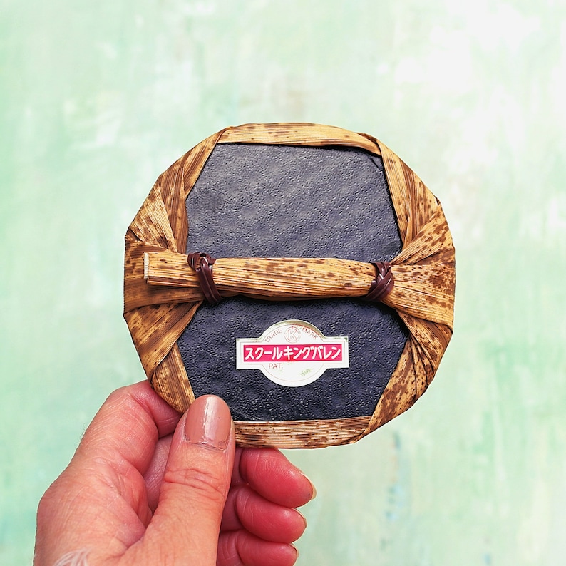 May include: A round, dark brown, woven, straw-like container with a black, circular, flat surface inside. The container has a red and white label that reads "TRADE MARK" and "スールキンプレン PAT."