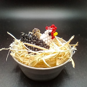 May include: A beaded hen figurine with black and white body, red comb, and yellow wattle, nestled in a small metal bowl filled with straw. The hen is a decorative item, possibly a collectible or a unique home accent.