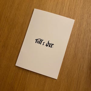 May include: A white card with the words "Till I Die" written in black calligraphy.
