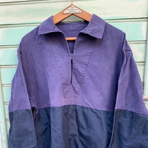 May include: A purple and black long-sleeved shirt with a V-neck collar. The shirt is made of a thick, textured fabric.