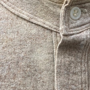 Puede incluir: Primer plano de una camisa de lino beige con cuello abotonado y un solo bot&oacute;n en la parte superior.