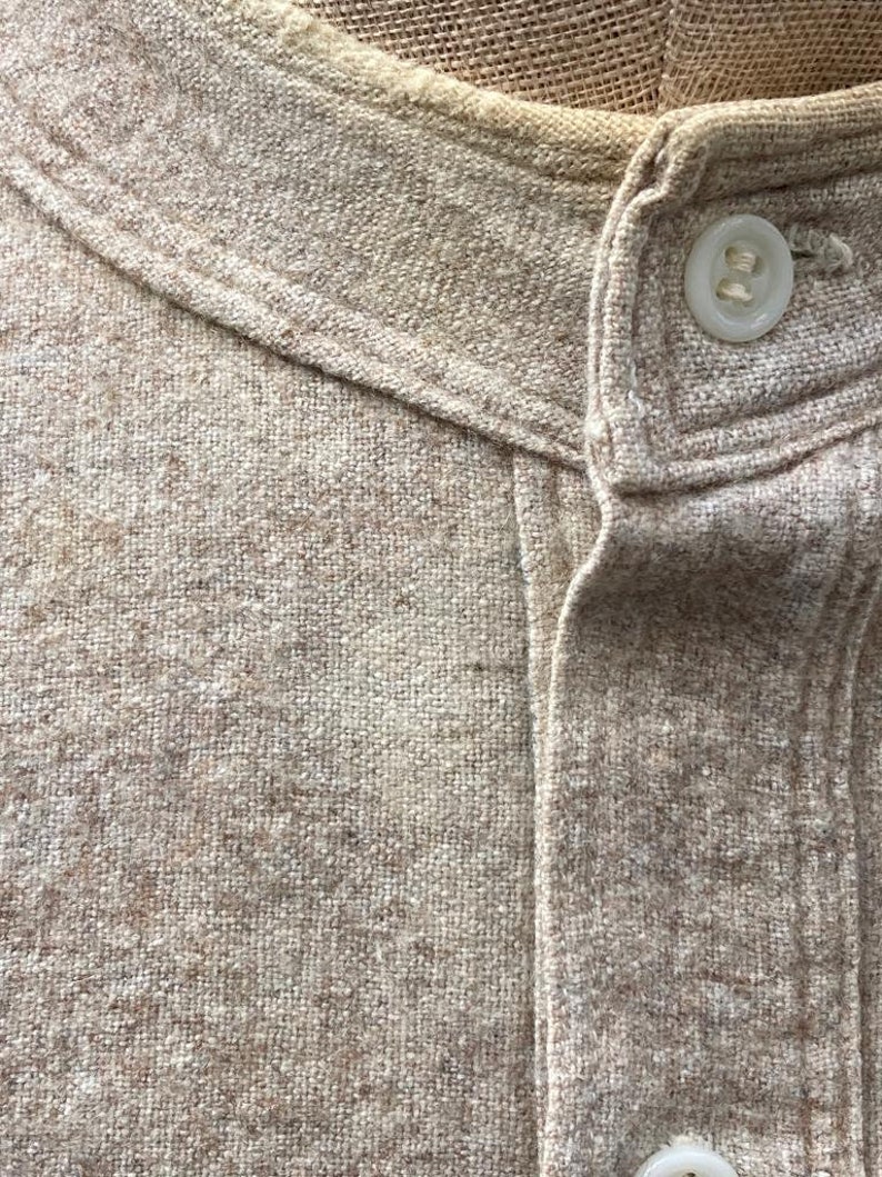 Puede incluir: Primer plano de una camisa de lino beige con cuello abotonado y un solo bot&oacute;n en la parte superior.