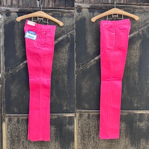 Puede incluir: Un par de pantalones vaqueros Levi's de color rosa colgados de una percha de madera. Los vaqueros tienen una pierna recta y un diseño clásico de cinco bolsillos. Los vaqueros tienen una etiqueta de Levi's unida al bolsillo trasero.