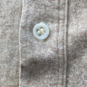 Puede incluir: Primer plano de un bot&oacute;n blanco cosido en una camisa de tela beige.