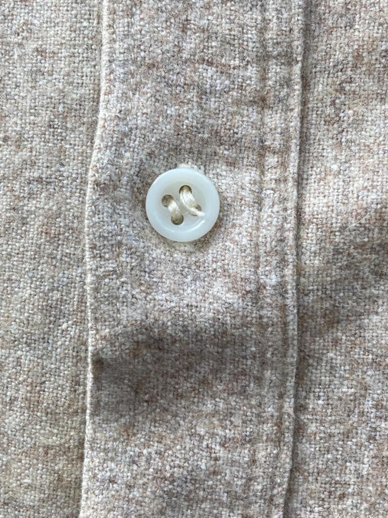 Puede incluir: Primer plano de un bot&oacute;n blanco cosido en una camisa de tela beige.