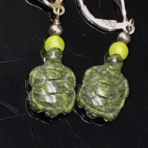 May include: A pair of silver dangle earrings with green turtle charms and yellow beads.