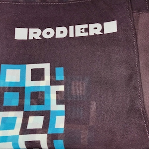 May include: A brown fabric bandana with a white geometric pattern and the text "RODIERI" in white.