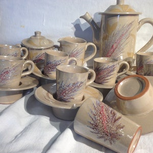 Puede incluir: Un juego de tazas y platillos de té de cerámica beige con un diseño floral. El juego incluye una tetera, una jarra de crema y un azucarero.