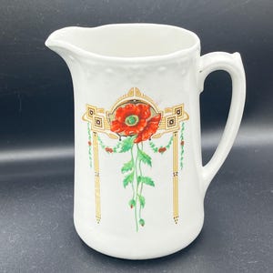 May include: White ceramic pitcher with a red poppy floral design. The pitcher features a curved handle and a spout for pouring. The poppy design includes green leaves and gold accents, adding a touch of elegance to the piece.