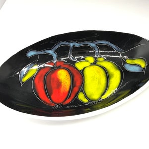 Può includere: Un piatto ovale in ceramica nera con finitura lucida presenta un disegno dipinto di due frutti, uno rosso e uno giallo, su una vite.