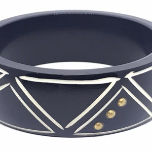 Puede incluir: Pulsera negra de bangle con diseños geométricos blancos y detalles dorados.