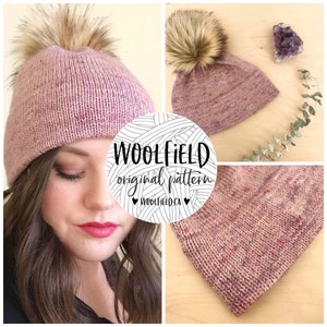 Op de afbeelding: Een roze gebreide beanie met een pluche pompon. De beanie is gemaakt van een gespikkeld garen en heeft een eenvoudig, klassiek ontwerp. De beanie wordt getoond op een model en op een houten oppervlak.