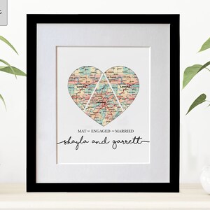 May include: A framed print with a heart-shaped map design. The map is divided into three sections, each representing a different stage of a relationship: "MAT", "ENGAGED", and "MARRIED". The names "shayla and garrett" are written below the map.