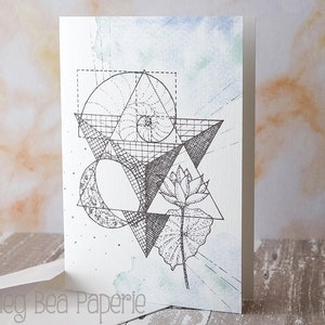 Peut inclure: Un design géométrique noir et blanc avec une fleur de lotus et une spirale. Le design est sur une carte blanche avec un fond aquarelle bleu clair.