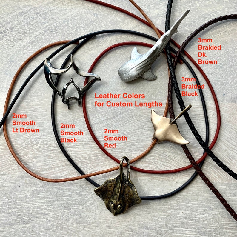 May include: A variety of leather cord necklaces with different styles of pendants, including a manta ray, a whale shark, and a stingray. The cords are available in black, brown, and red, and the pendants are available in silver and gold. The text "Leather Colors for Custom Lengths" is visible in the image.