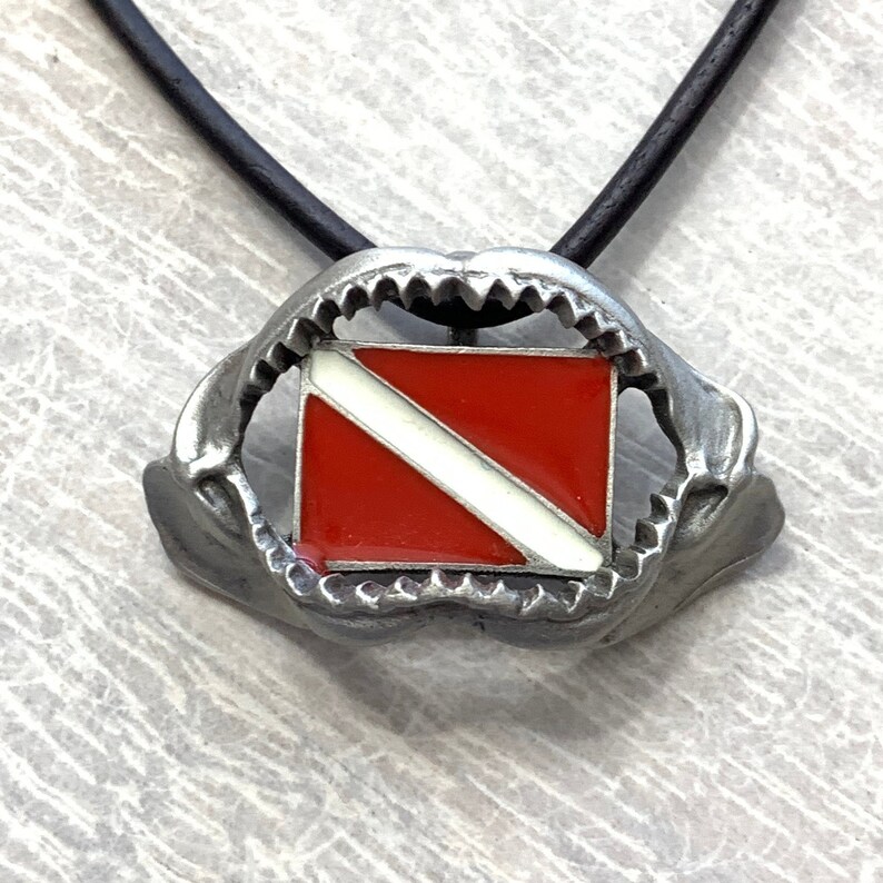 May include: A silver shark jaw pendant necklace with a red and white scuba diving flag inside the jaws.