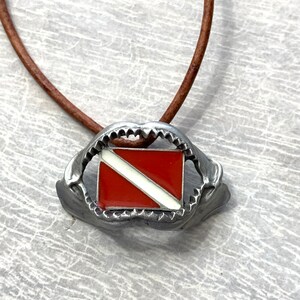 May include: A silver necklace with a shark tooth pendant featuring a red and white scuba diving flag.