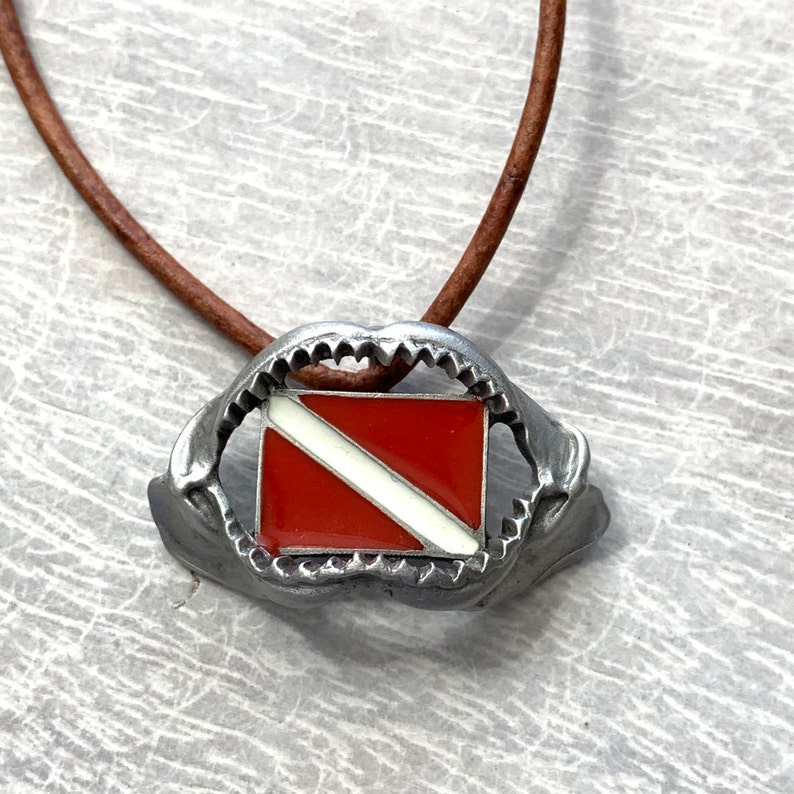 May include: A silver necklace with a shark tooth pendant featuring a red and white scuba diving flag.
