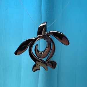 May include: A silver-toned turtle pendant necklace. The turtle is stylised and has a smooth, shiny finish.