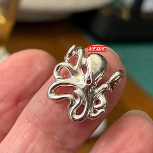 May include: A silver-toned octopus pendant with a polished finish and curved tentacles. The charm features a small loop at the top for attachment. A red rectangular label on the piece displays the text 3/4"X3/4" indicating its dimensions.